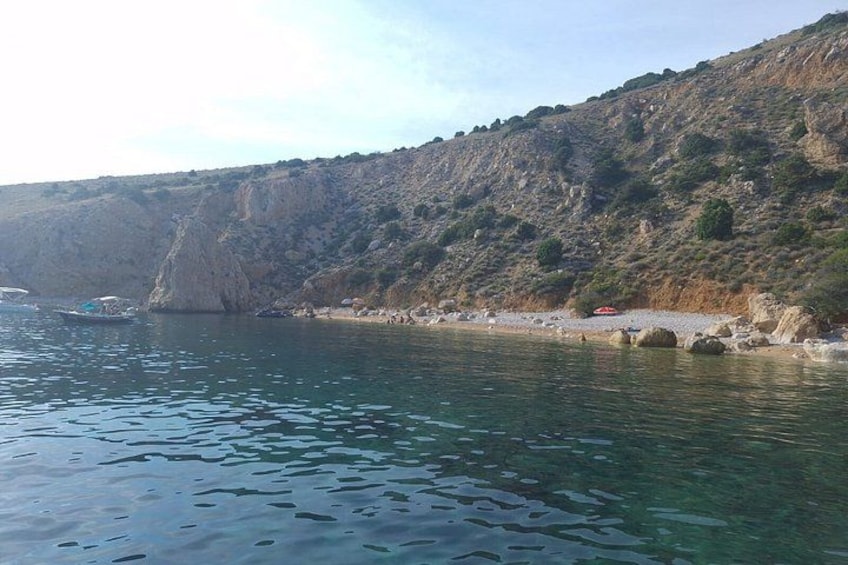 A coastal landscape with clear water, rocky cliffs, and a beach. 2