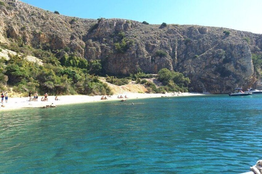 A beach with people sunbathing and swimming, surrounded by rocky cliffs and clear blue water. 2