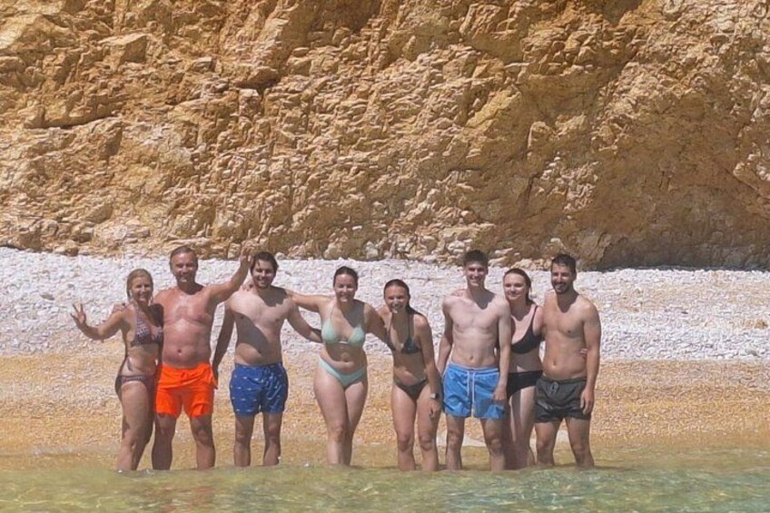 A group of people standing in shallow water with a rocky cliff in the background. 1