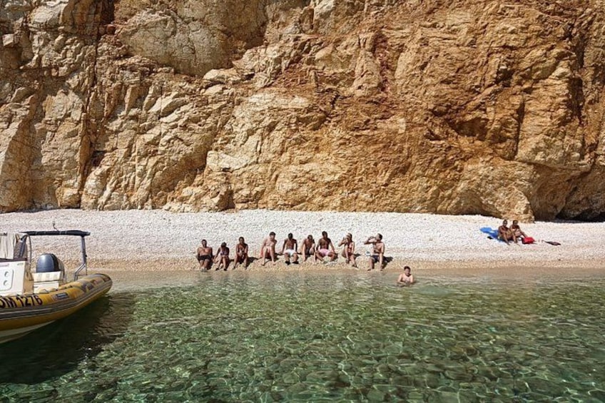 A group of people on a beach with a rocky cliff in the background and a boat in the water. 2