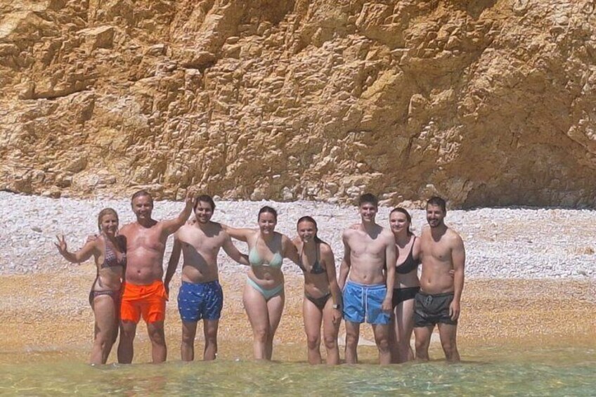 A group of people standing in shallow water with a rocky cliff in the background. 1