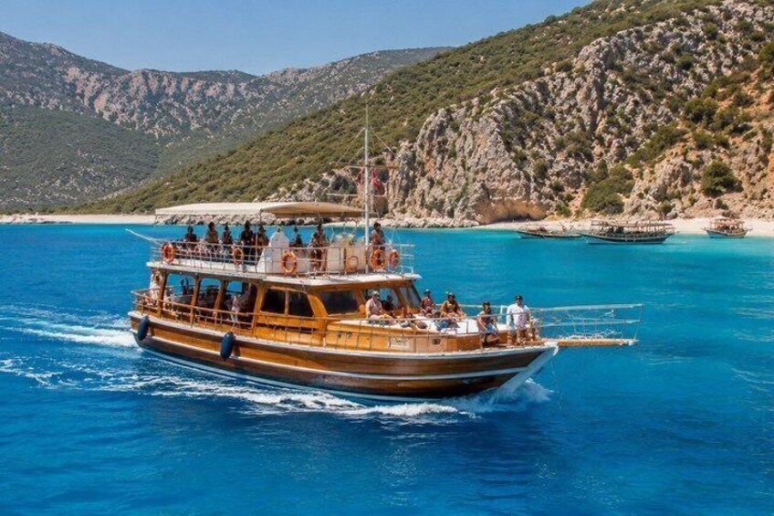 A wooden boat with passengers on a clear blue sea, surrounded by rocky hills. 4