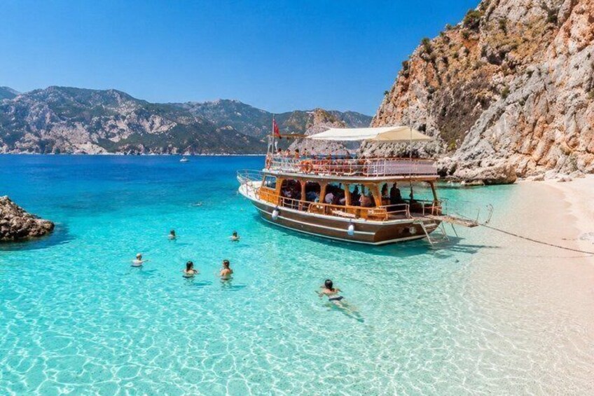 A boat with passengers near a clear turquoise beach with rocky cliffs in the background. 5