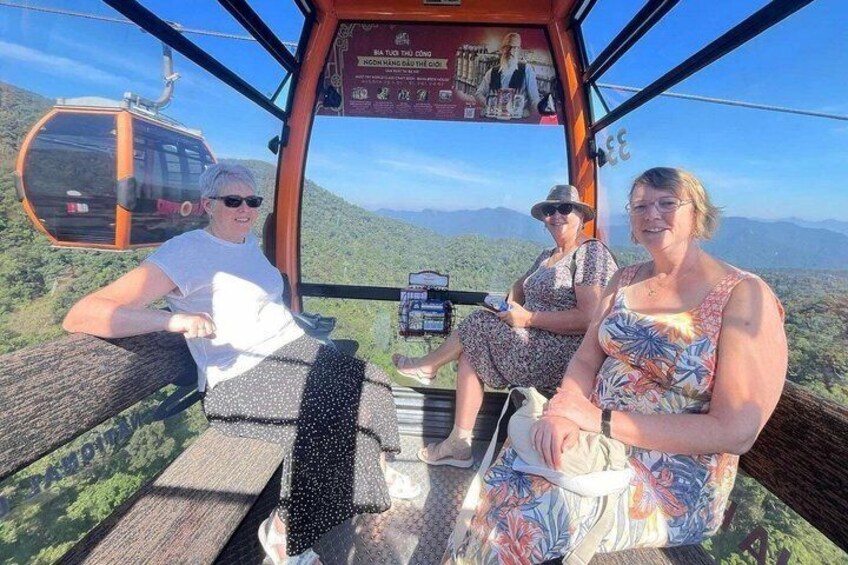 Three people seated in a cable car with a mountainous landscape in the background. 3