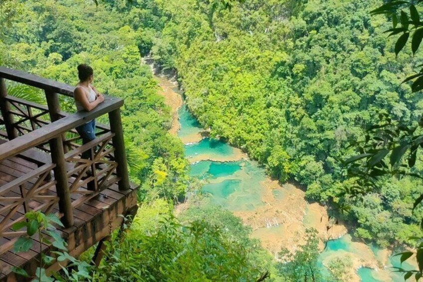 A person on a wooden deck overlooking a river surrounded by dense greenery. 1
