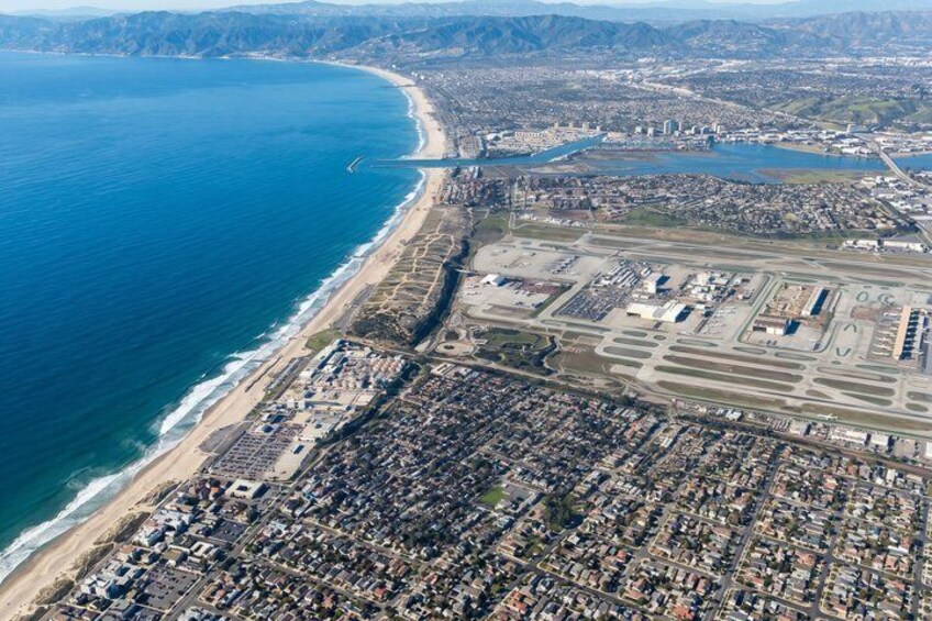 An aerial view of a coastal city with a beach, a large airport, and dense urban development. 4
