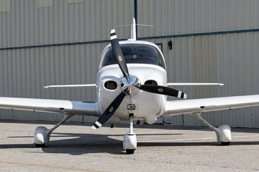 A small propeller airplane parked on a tarmac with a hangar in the background. 5