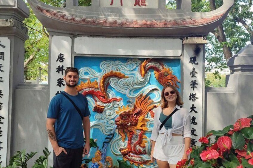 Two people standing in front of a dragon mural with Chinese characters. 1