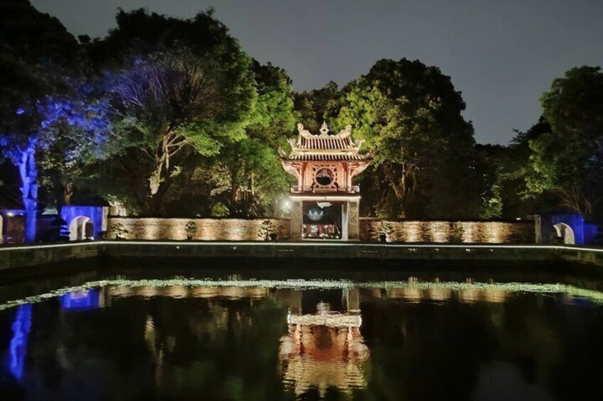 A traditional pavilion with a reflection in a pond, surrounded by trees and illuminated by blue lighting. 2