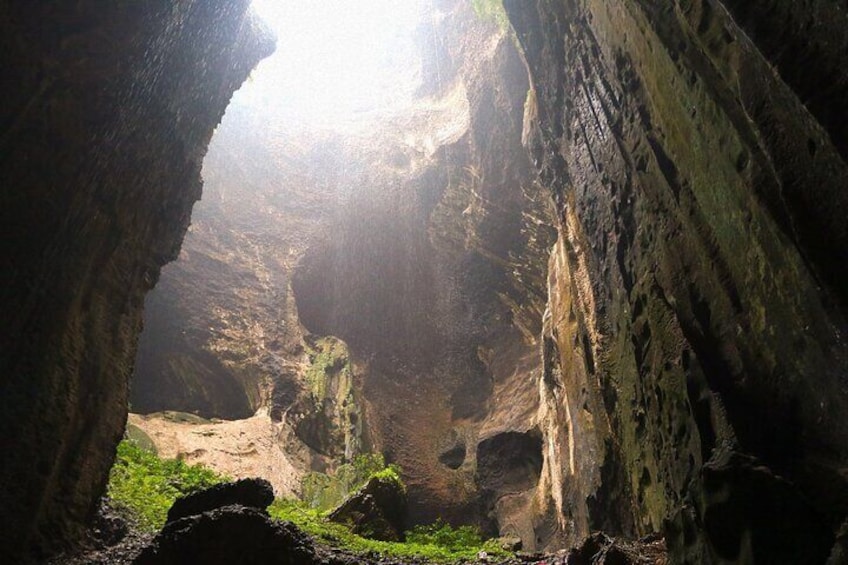 A cave with sunlight streaming through an opening, rocky walls, and green moss. 1