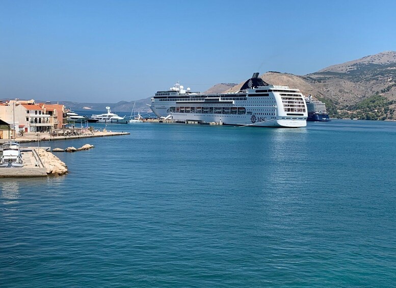 A large cruise ship docked at a port with smaller boats nearby, surrounded by a hilly landscape and clear skies. 1