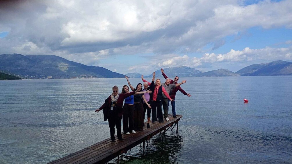 A group of people on a wooden dock extending into a calm lake with mountains in the background. 5