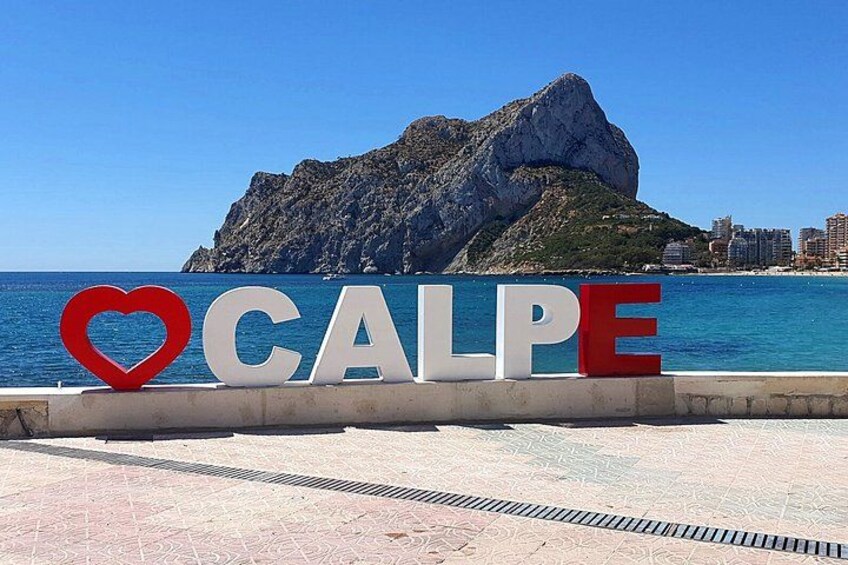 A sign with 'CALPE' and a heart symbol, a rocky mountain, and a coastline. 3