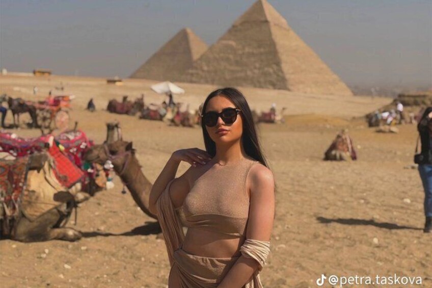 A person standing in a desert with camels and pyramids in the background. 2