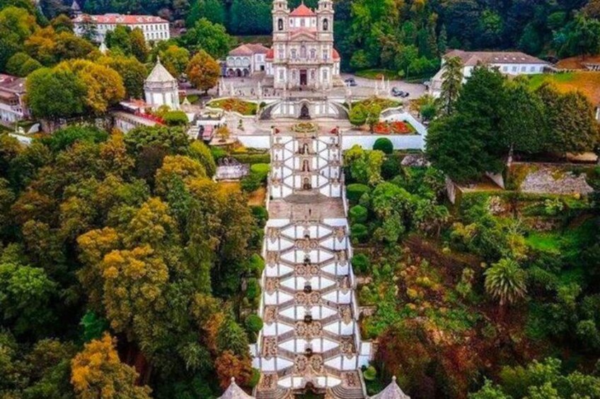 A historic building with a tower and intricate roof design, surrounded by lush greenery and other structures. 1