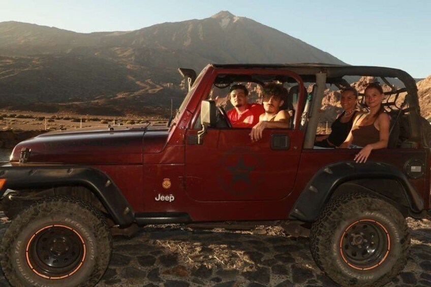 A red Jeep with four passengers, parked on a rocky terrain with mountains in the background. 1