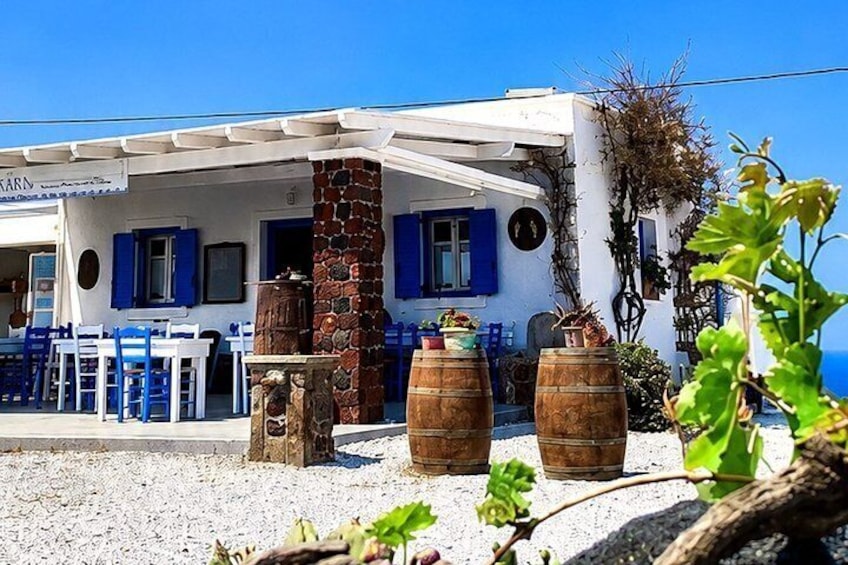 A white building with blue shutters, wooden barrels, and a gravel ground. 4