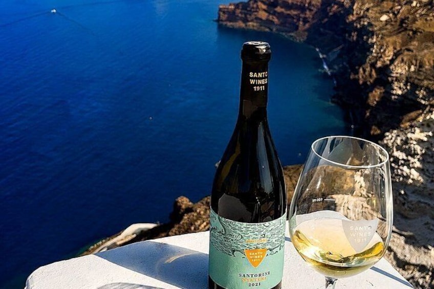 A bottle of Santo Wines 1911 and a glass of white wine on a table with a coastal view. 5