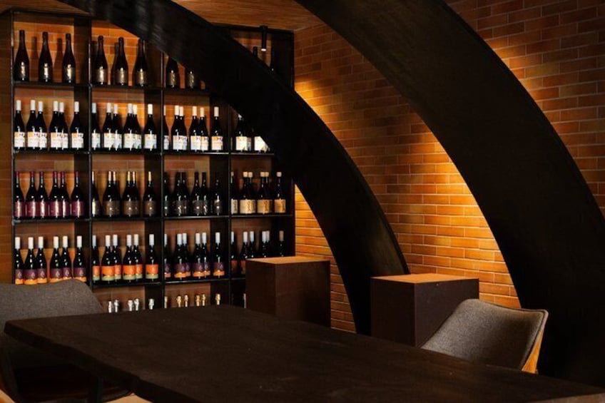 A wine cellar with shelves of bottles, a wooden table, and curved brick walls. 1