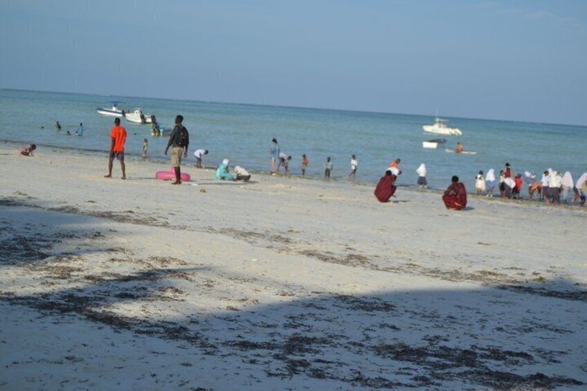 A beach with people sunbathing and swimming, boats in the water, and a clear sky. 5