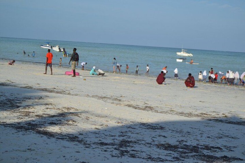 A beach with people, boats, and seaweed on the sand. 5