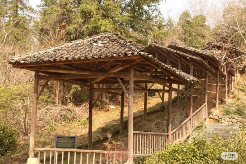 A wooden gazebo with a tiled roof, surrounded by trees and a stone pathway. 2