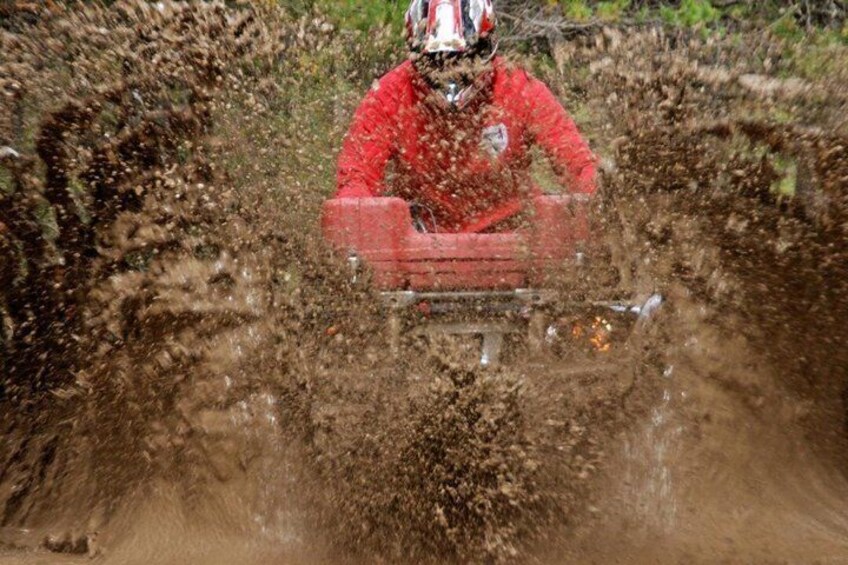 A person riding a red ATV on a muddy trail. 2