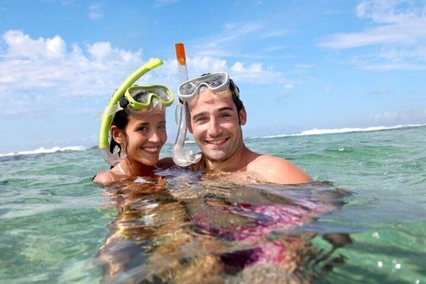 Two people snorkeling in clear ocean water with a rocky seabed. 3