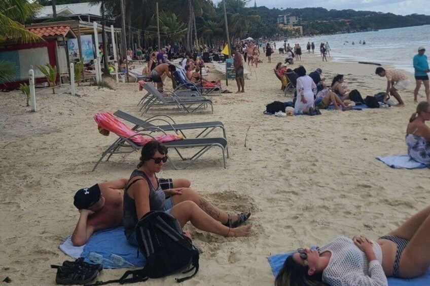 A crowded beach with people sunbathing, lounging on chairs, and walking along the shore. 2
