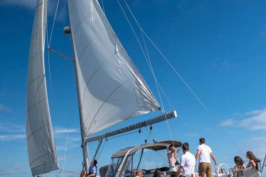 A sailboat with people on deck, a clear blue sky, and a calm sea. 1