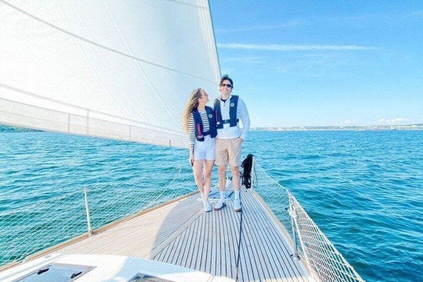 A couple on a sailboat with a clear blue sea and a distant shoreline. 4