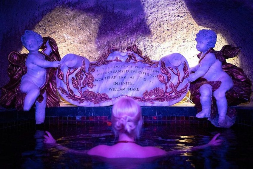 A statue of a cherub holding a plaque with a quote, a pool, and a person in the water. 1