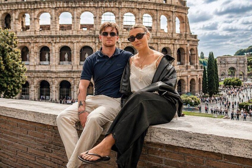 A couple sitting on a ledge with the Colosseum in the background. 1