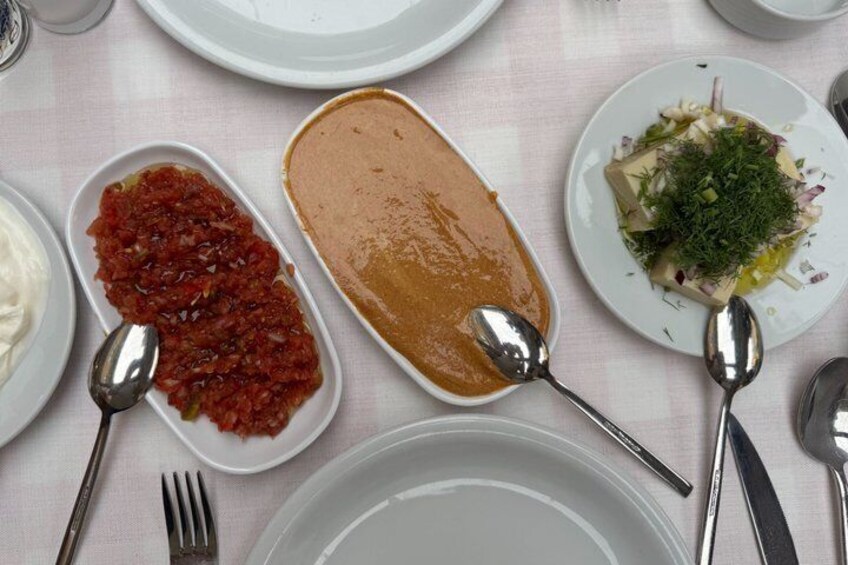 A table with plates of food, including a red sauce, a brown spread, and a salad with greens. 3