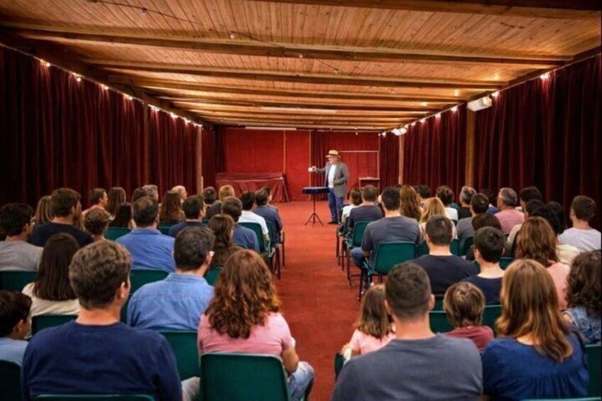 An indoor auditorium with rows of green chairs facing a stage with a speaker. 3