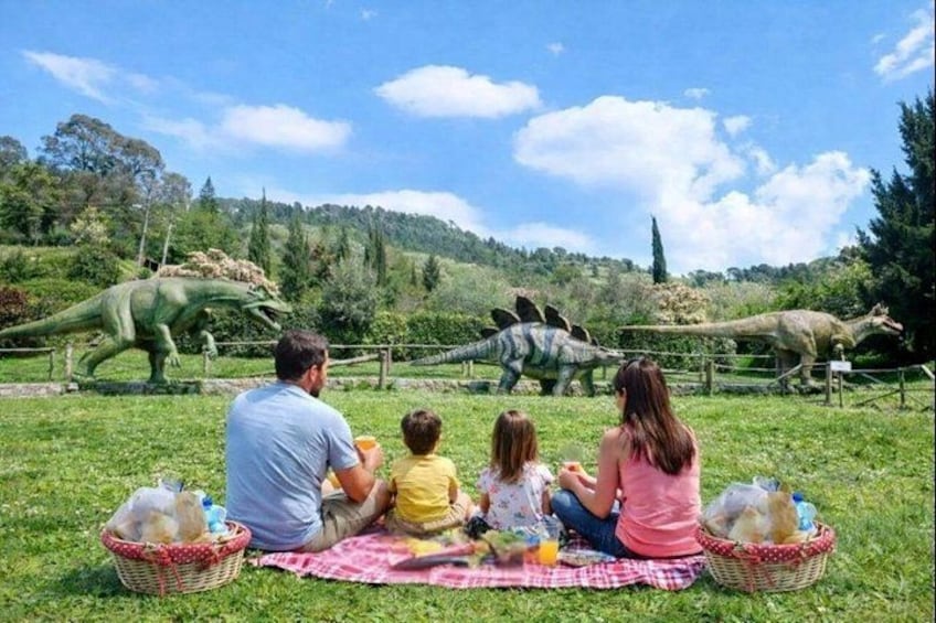 A family picnic on grass with dinosaurs in the background. 1