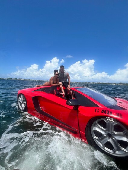 A red sports car on water with a clear sky and distant buildings. 1