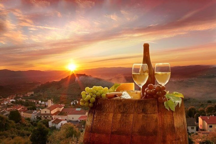 A wooden barrel with wine glasses and grapes, set against a sunset over a village. 1