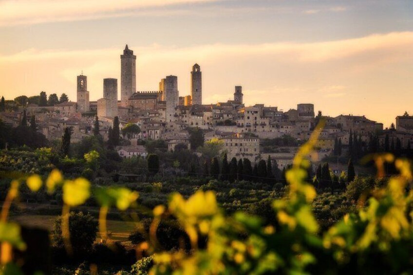 A historic cityscape with prominent towers and a castle, set against a sunset sky. 2