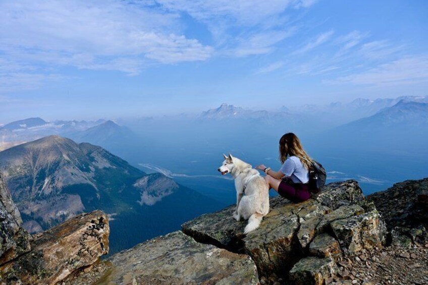 A person sitting on a rocky outcrop with a dog, overlooking a mountainous landscape and a body of water. 4