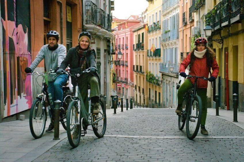 Three people riding bicycles on a cobblestone street in a European town. 1