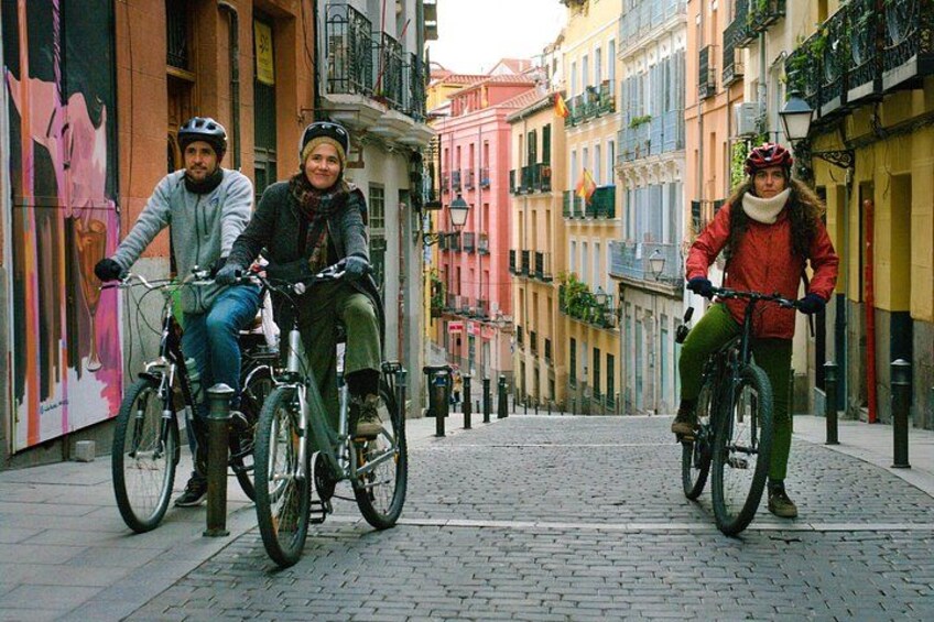 Three people riding bicycles on a cobblestone street in a European town. 1