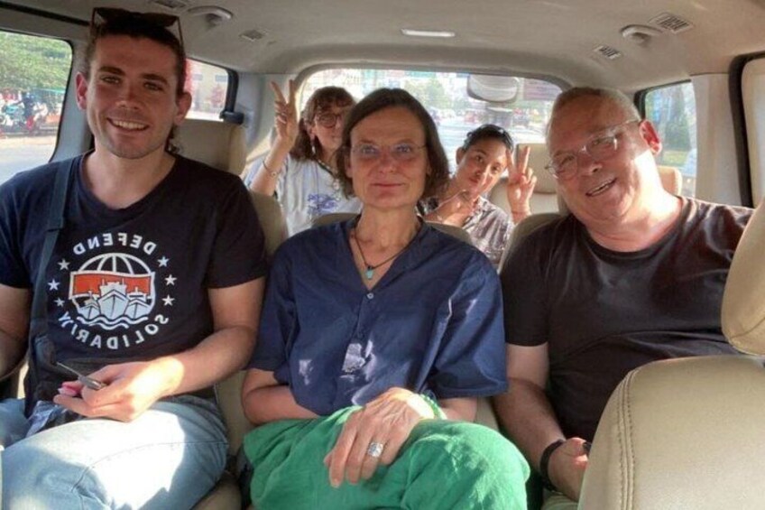 Three people seated in a vehicle with a visible logo on the man's t-shirt. 2