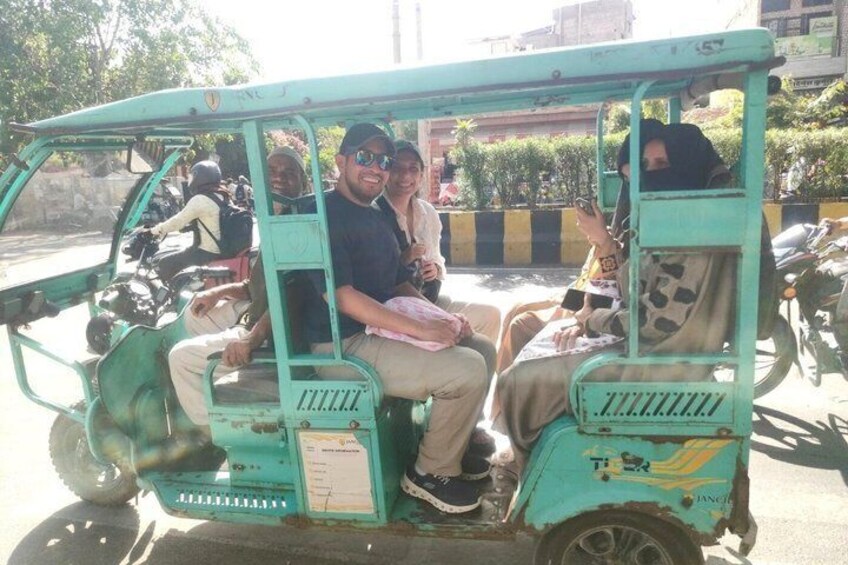 A teal auto-rickshaw with passengers, parked on a street with other vehicles and greenery in the background. 5