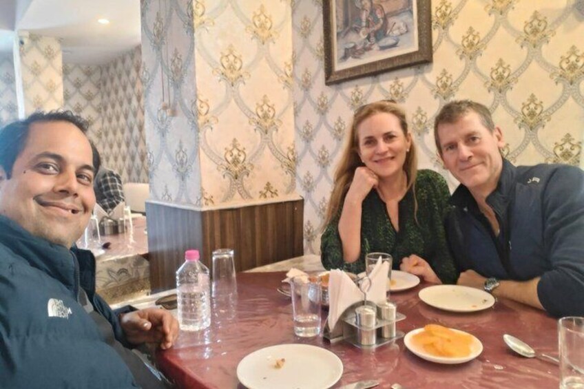 Three people seated at a table in a restaurant with patterned wallpaper and a painting on the wall. 3