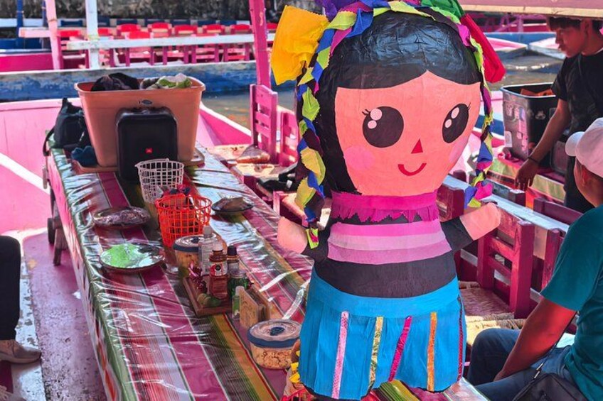 A colorful table with a large doll, a basket, and various items on it. 5