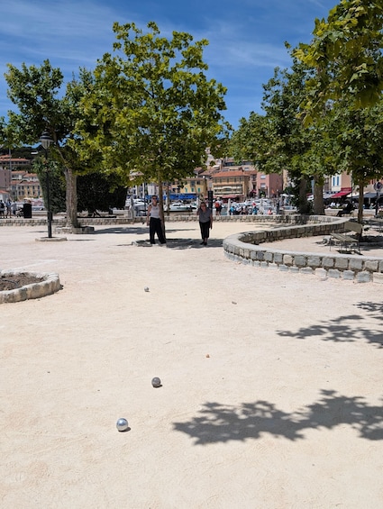 A sandy open space with trees, benches, and people walking. 5