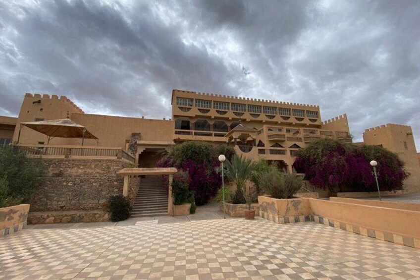 A historic building with a checkered courtyard, surrounded by lush greenery and under a cloudy sky. 4
