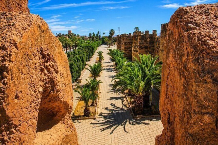 A pathway flanked by large rock formations, lined with palm trees and a clear blue sky. 2