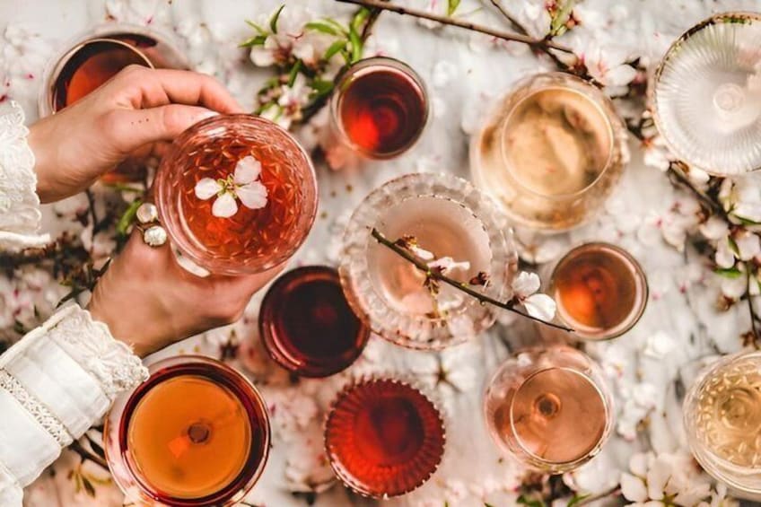 A person holding a glass with a flower, surrounded by various glasses of beverages on a table with flowers. 1